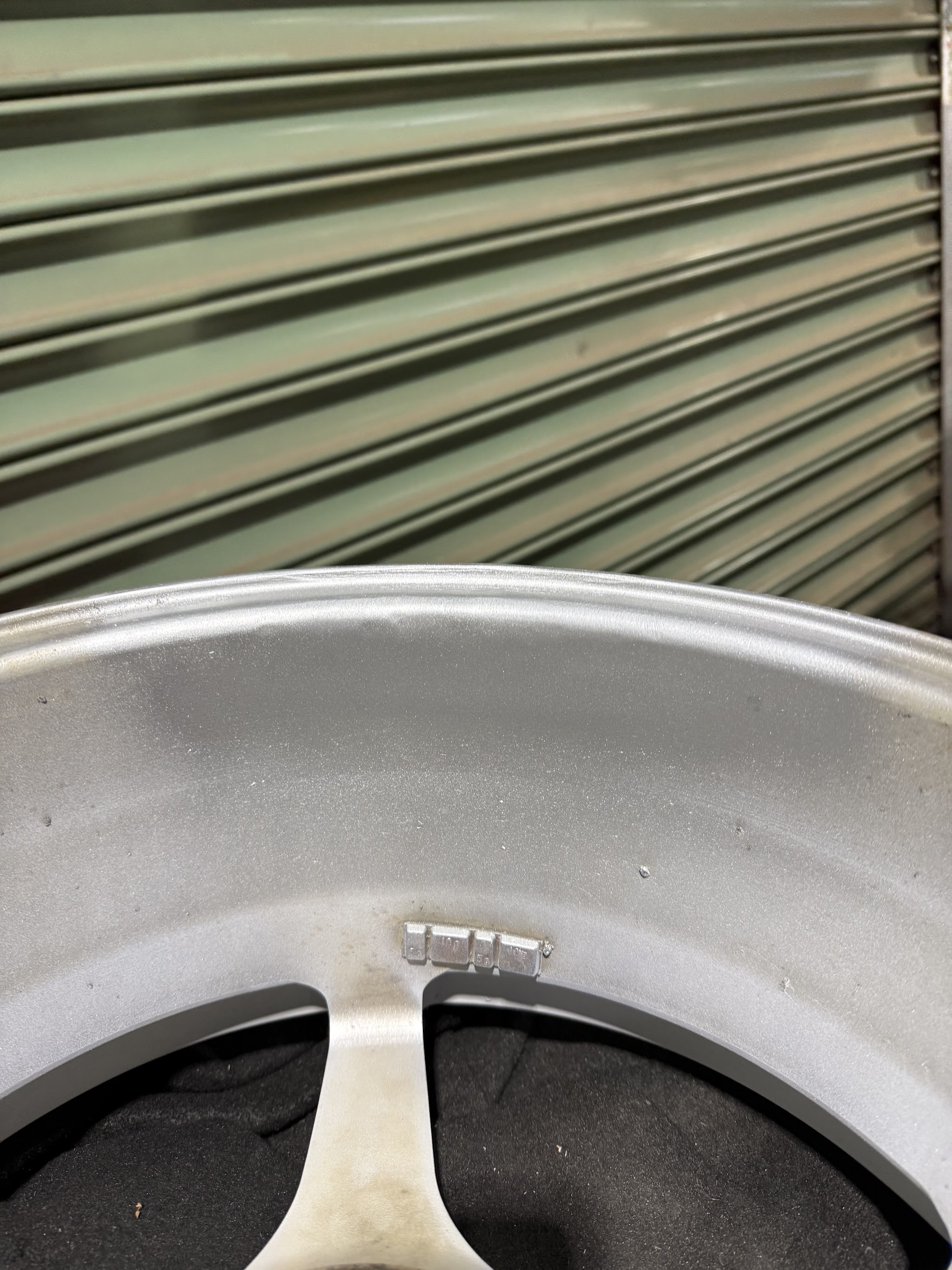 Machined alloy wheel face with balance weights refitted, in front of the workshop roller door